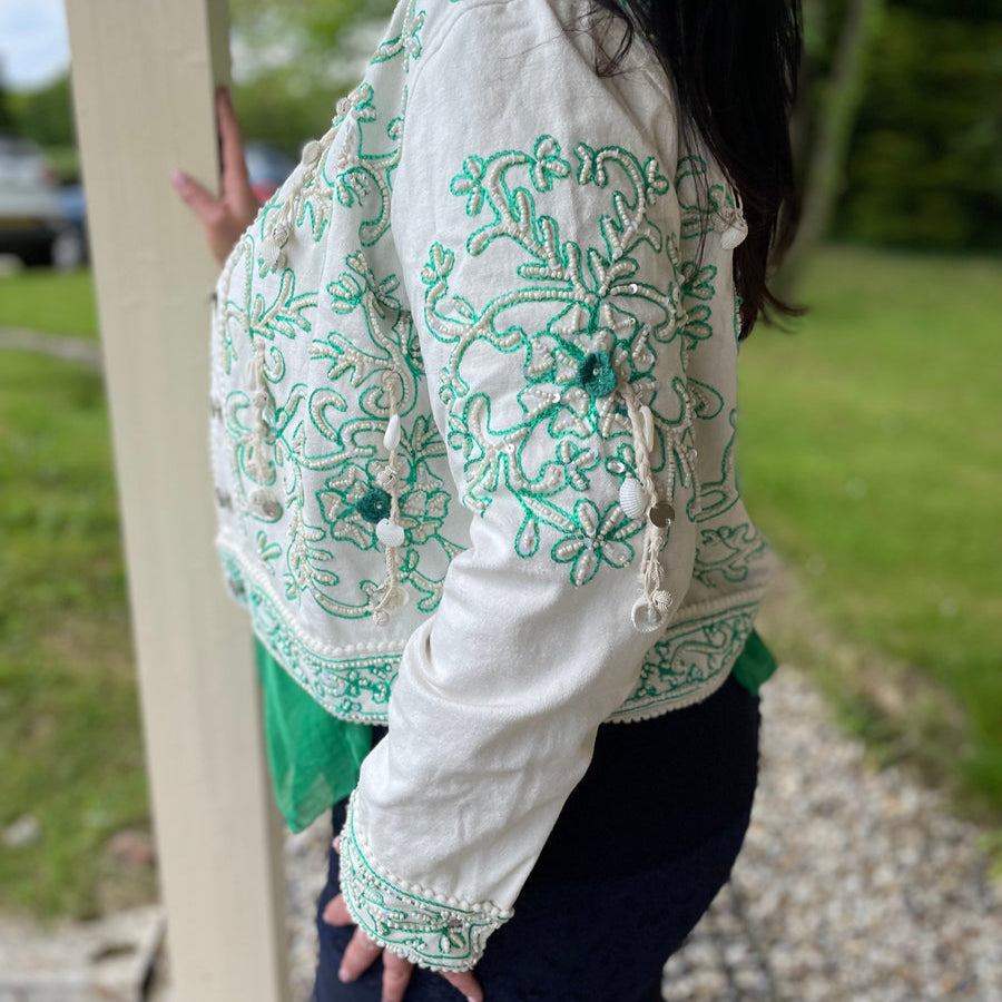 Modelo luciendo una chaqueta boho blanca con bordados turquesa en un entorno natural.