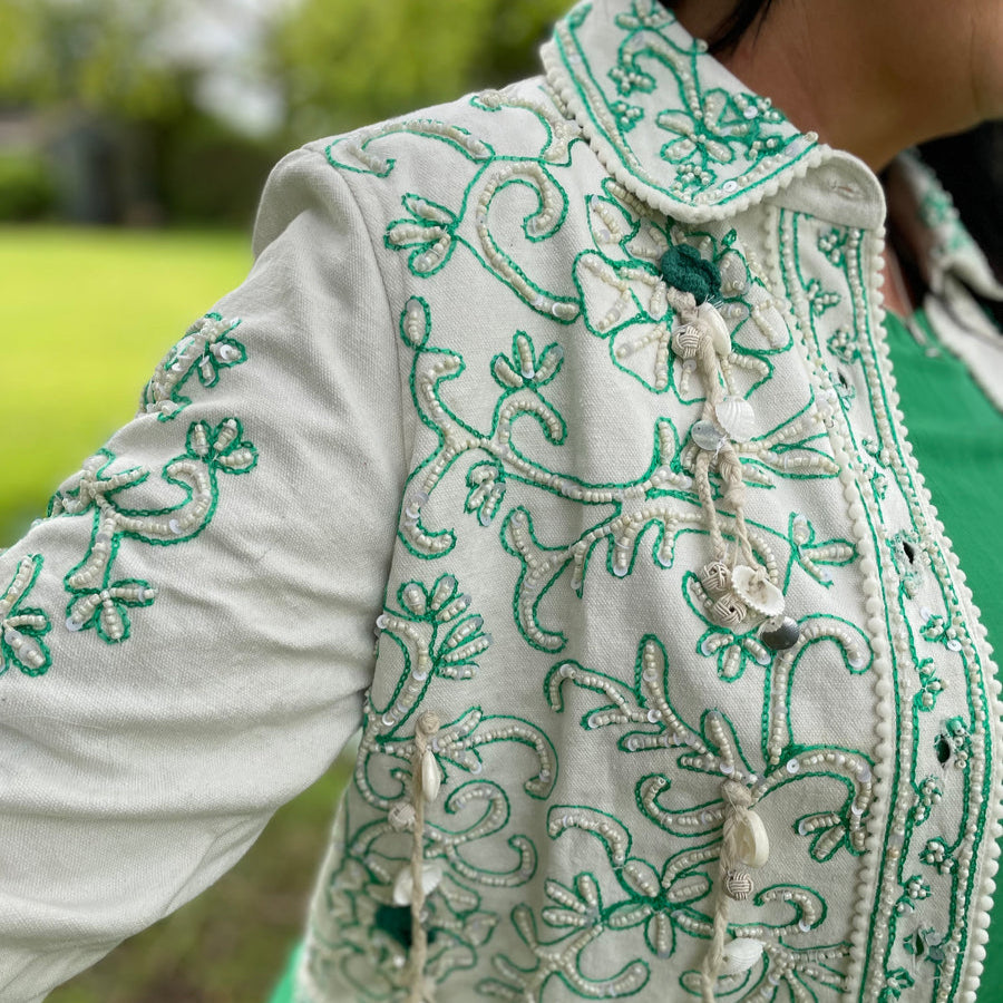 Modelo luciendo una chaqueta boho blanca con bordados turquesa en un entorno natural.